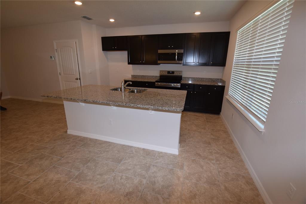 A kitchen features dark cabinets, granite countertops, a central island, and tile flooring — 9496 BAUER ALLEY, WINTER GARDEN, FL