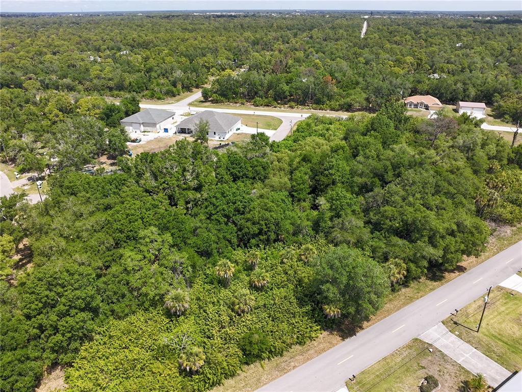 An aerial view shows a wooded lot bordered by a paved road and nearby houses — 1181 EPPINGER DRIVE, PORT CHARLOTTE, FL