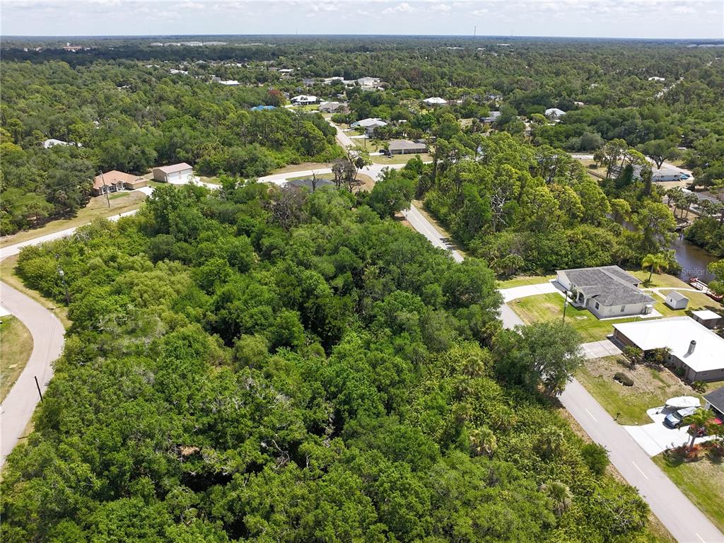 An aerial view shows a wooded lot surrounded by residential houses and paved roads — 1181 EPPINGER DRIVE, PORT CHARLOTTE, FL