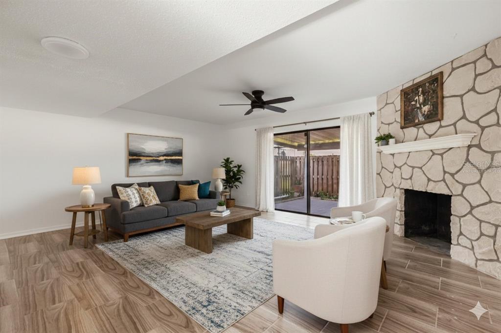 A living room features a stone fireplace, wood-look tile flooring, and a sliding glass door — 2250 S PALMETTO AVENUE UNIT i-11, DAYTONA BEACH, FL