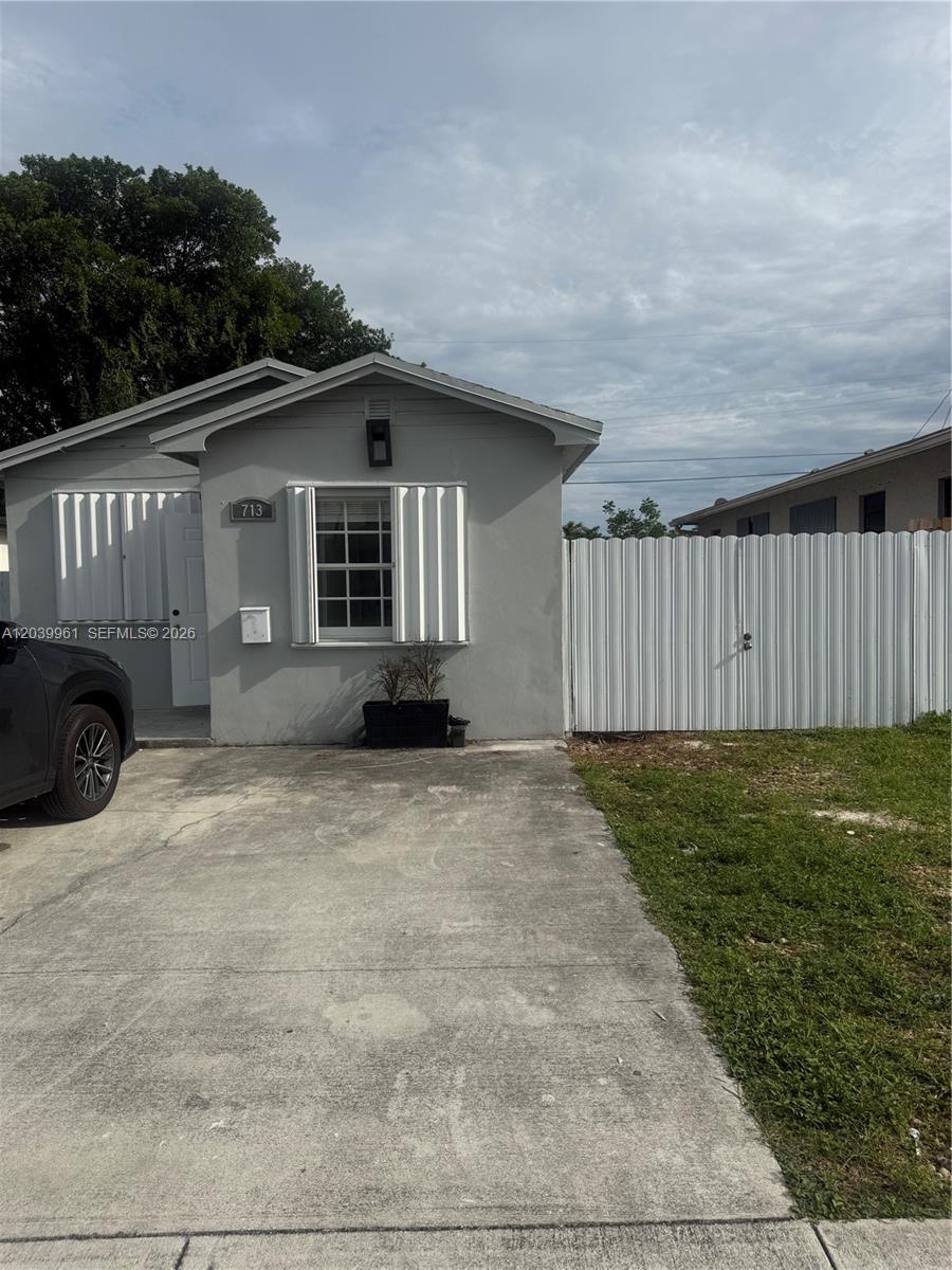 A gray single-story house features a concrete driveway, white shutters, and a metal privacy fence — 713 NW 4th St, Hallandale Beach FL 33009, HALLANDALE BEACH, FL