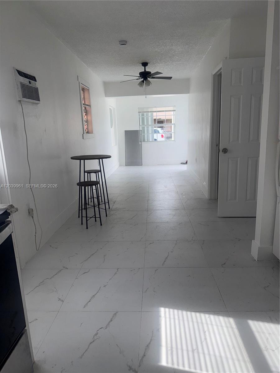 A narrow, white-walled room features marble-look tile flooring, a ceiling fan, and a small table — 713 NW 4th St, Hallandale Beach FL 33009, HALLANDALE BEACH, FL