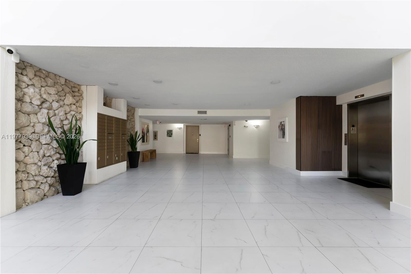 A modern building lobby features white tiled floors, a stone accent wall, and an elevator — 16200 Golf Club Rd # 102, Weston FL 33326, WESTON, FL