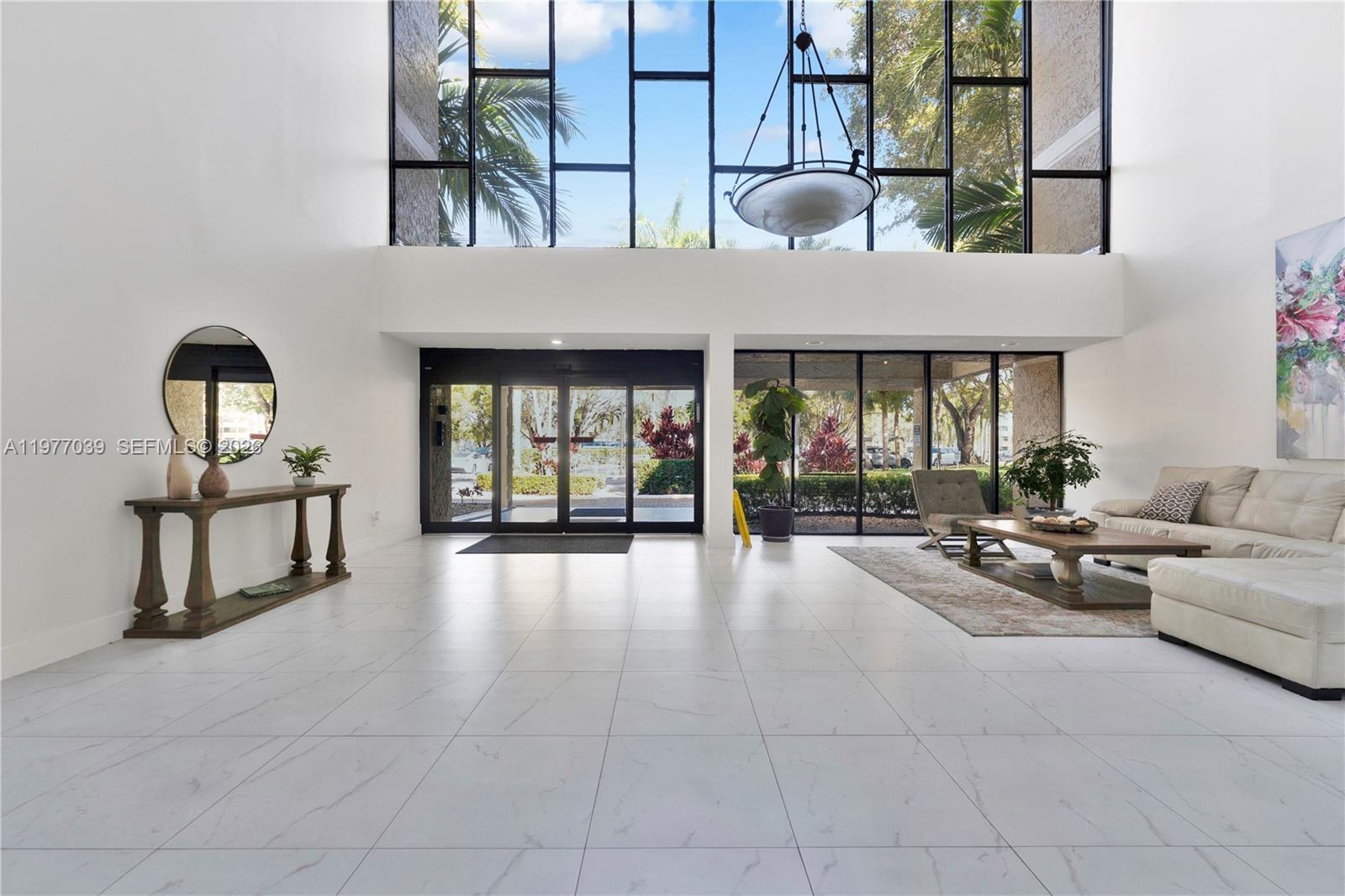 A spacious, high-ceilinged lobby features white tile floors, floor-to-ceiling windows, and a seating area — 16200 Golf Club Rd # 102, Weston FL 33326, WESTON, FL
