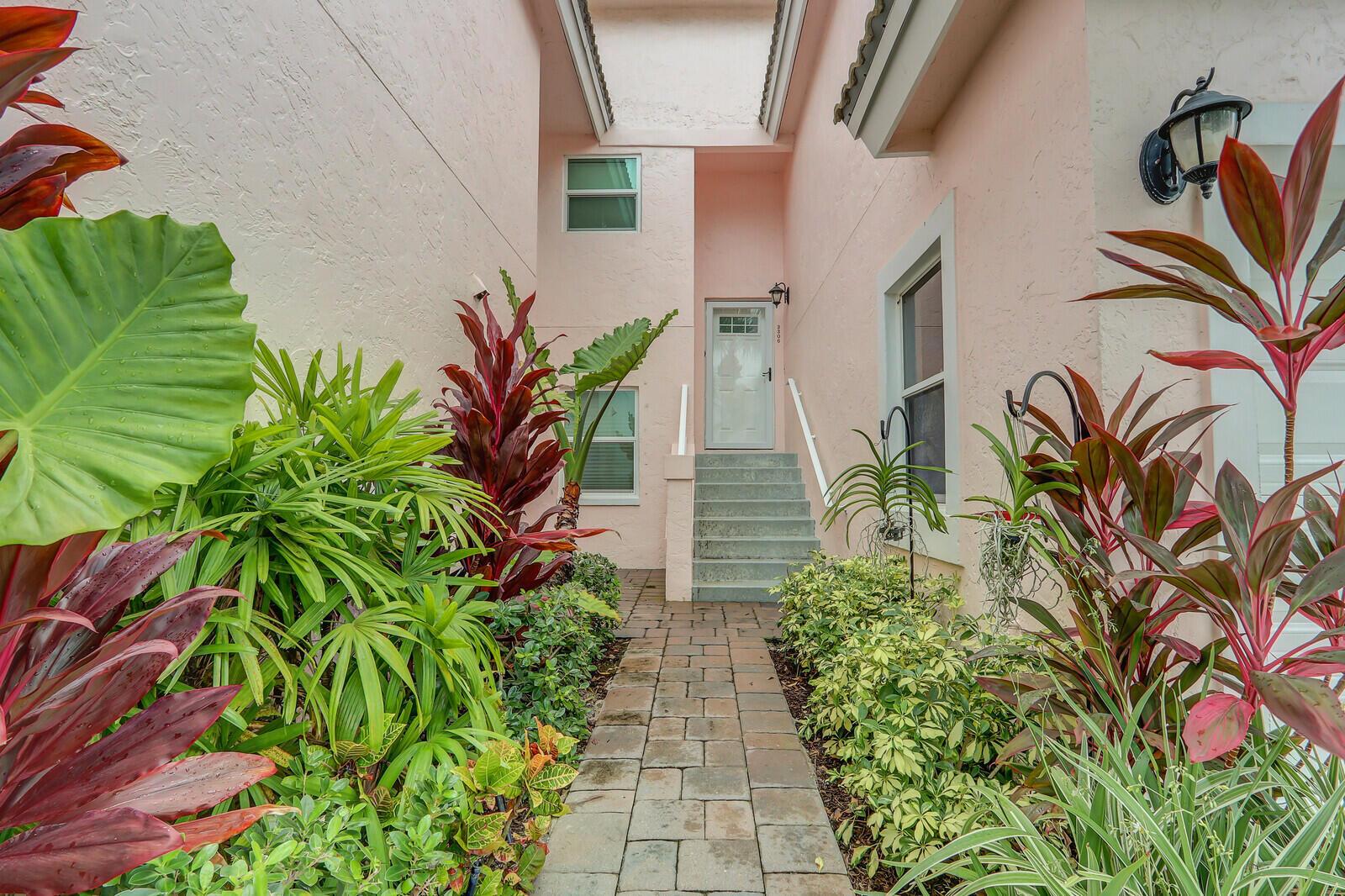 A stone walkway leads to the front entrance of a pink house with tropical landscaping — 3306 Fairway Drive N, Jupiter FL 33477, JUPITER, FL