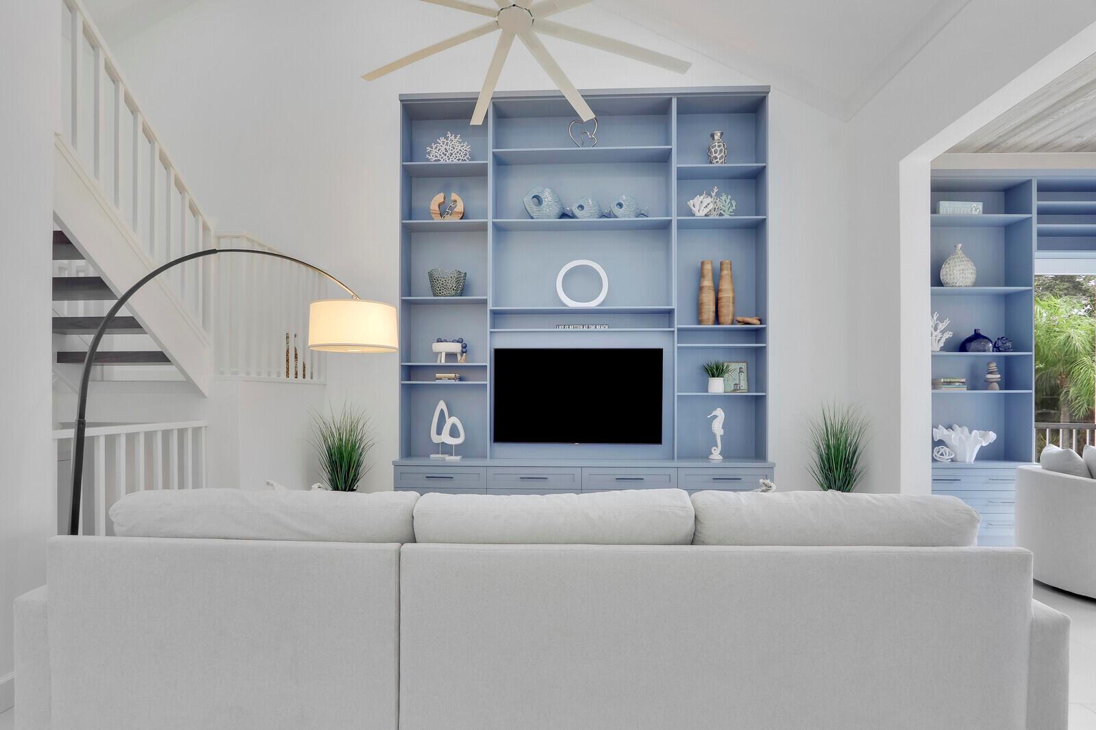 A living room features a large blue built-in shelving unit with a television and white sofa — 3306 Fairway Drive N, Jupiter FL 33477, JUPITER, FL