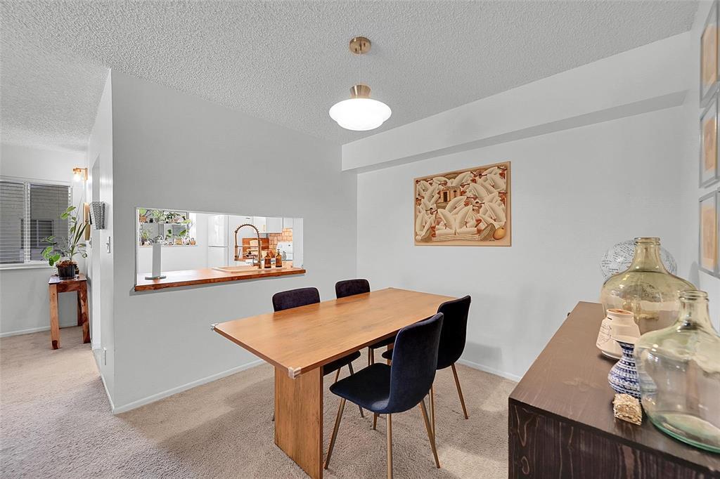 A dining room features a wooden table, dark chairs, and a pass-through window to the kitchen — 117 Gardens Drive # 204, Pompano Beach FL 33069, POMPANO BEACH, FL