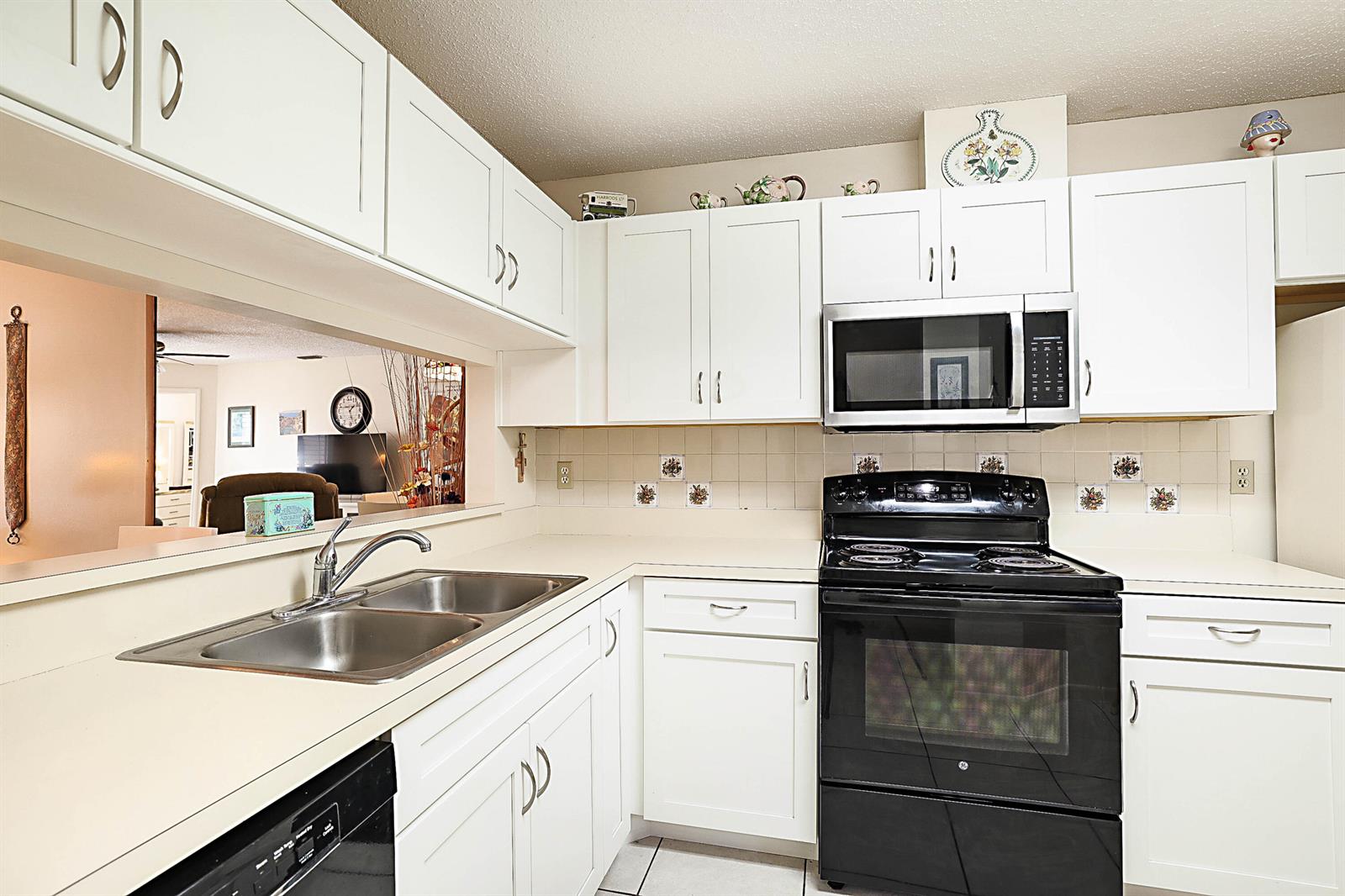 A kitchen features white cabinets, a black stove, a stainless steel sink, and tiled backsplash — 405 Harbour Pointe Way, FL 33413, FL