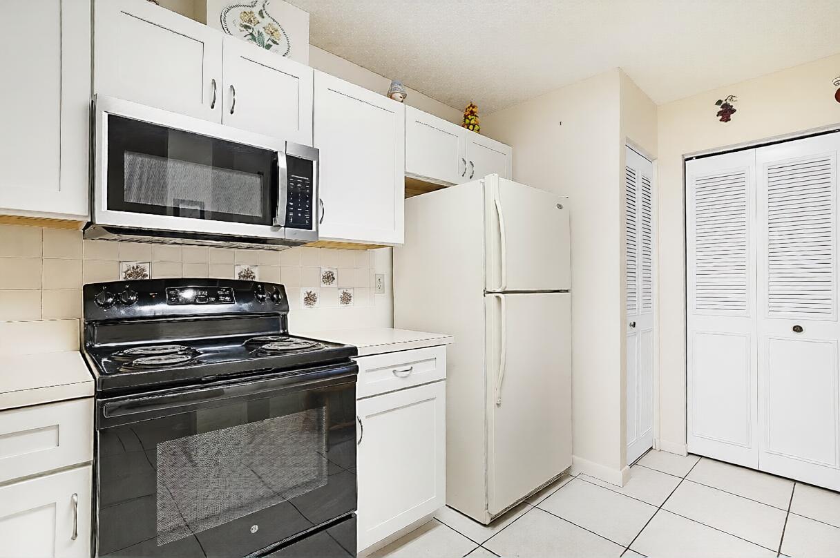 A kitchen features white cabinets, a black stove, a microwave, and a white refrigerator — 405 Harbour Pointe Way, FL 33413, FL