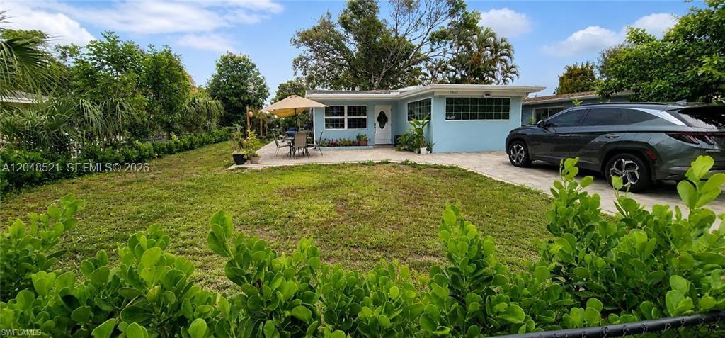 A light blue single-story house features a paved driveway and a patio with an umbrella — FORT MYERS, FL