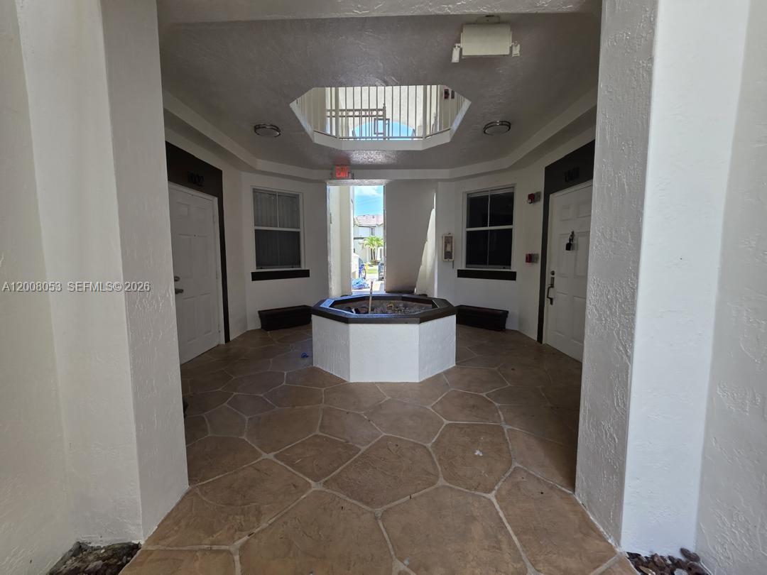 An outdoor courtyard features a central hexagonal planter, stone-patterned flooring, and two white entry doors — 8874 W Flagler St # 101, Miami FL 33174, MIAMI, FL