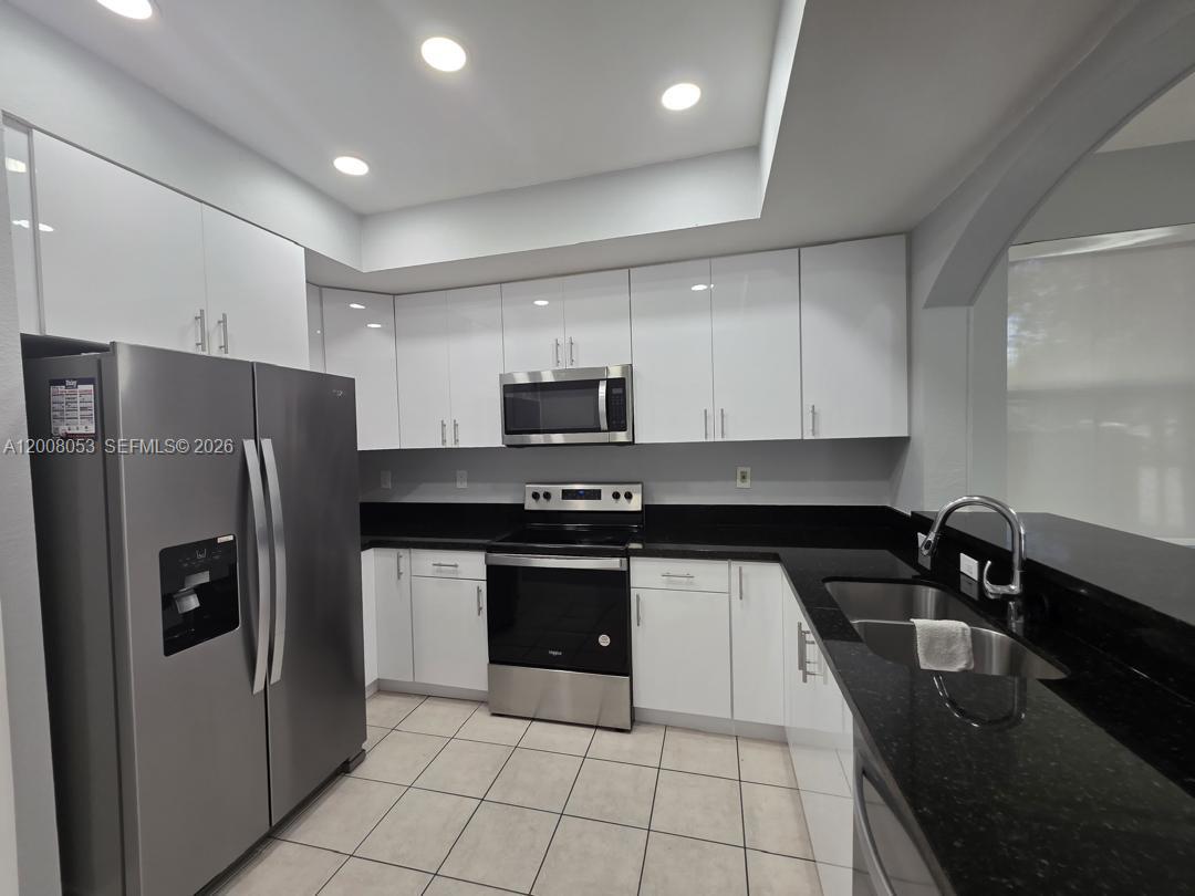A kitchen features white cabinets, black countertops, stainless steel appliances, and light-colored tiled flooring — 8874 W Flagler St # 101, Miami FL 33174, MIAMI, FL