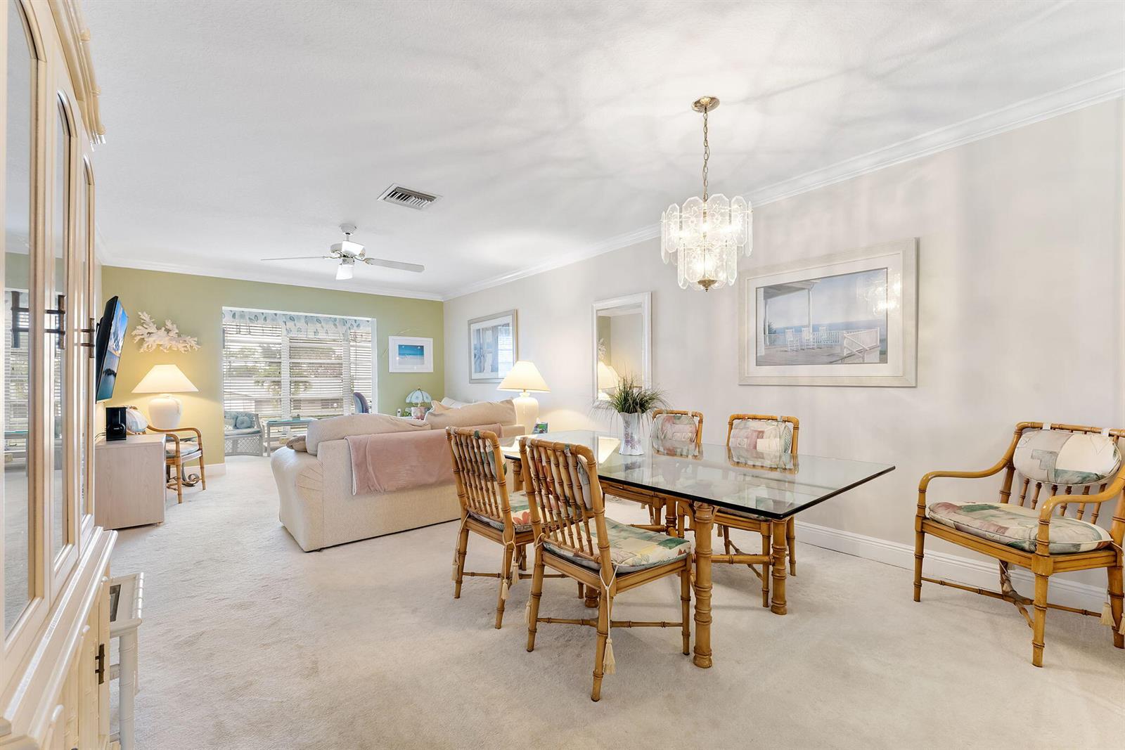 A dining area with a glass table and bamboo chairs sits beside a living room — 2401 Del-aire Boulevard E # 201, Delray Beach FL 33445, DELRAY BEACH, FL