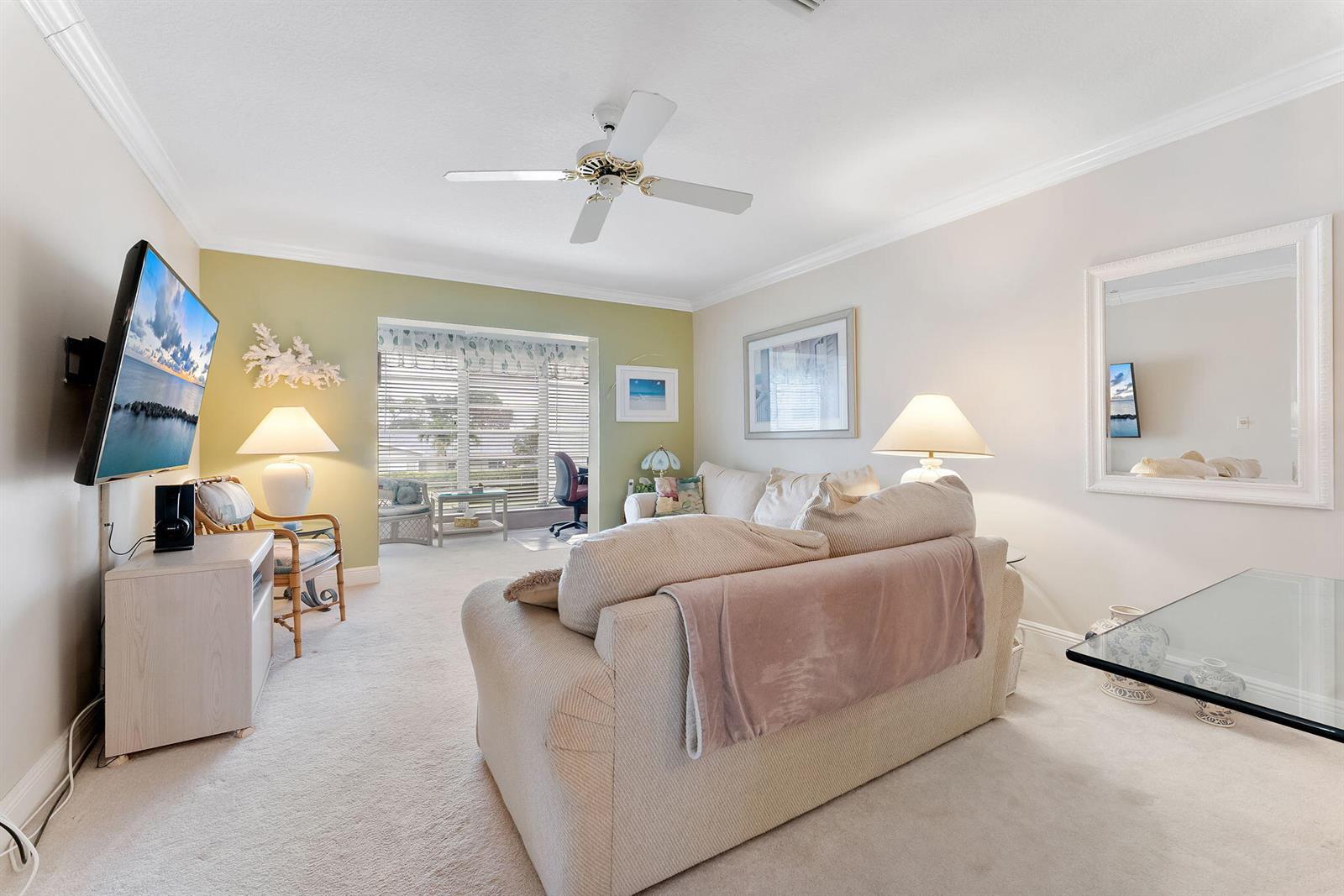 A living room features a beige sofa, a wall-mounted television, and a ceiling fan — 2401 Del-aire Boulevard E # 201, Delray Beach FL 33445, DELRAY BEACH, FL