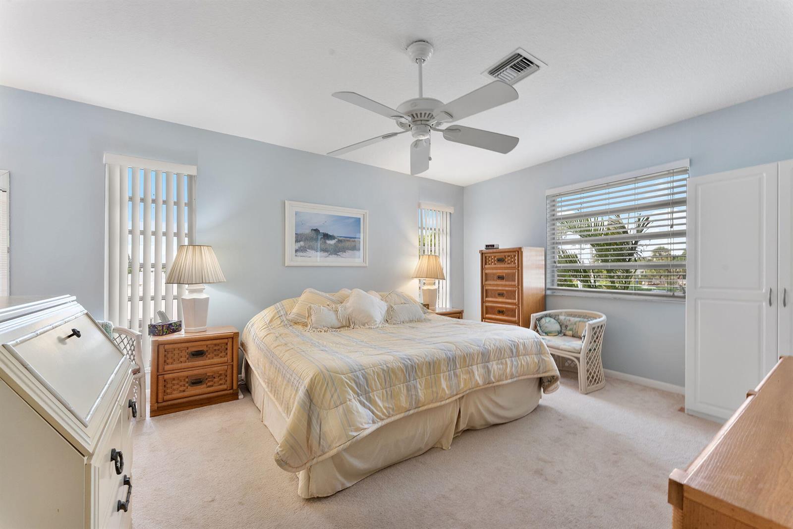 A bedroom features a king-sized bed, wicker furniture, light blue walls, and beige carpeting — 2401 Del-aire Boulevard E # 201, Delray Beach FL 33445, DELRAY BEACH, FL