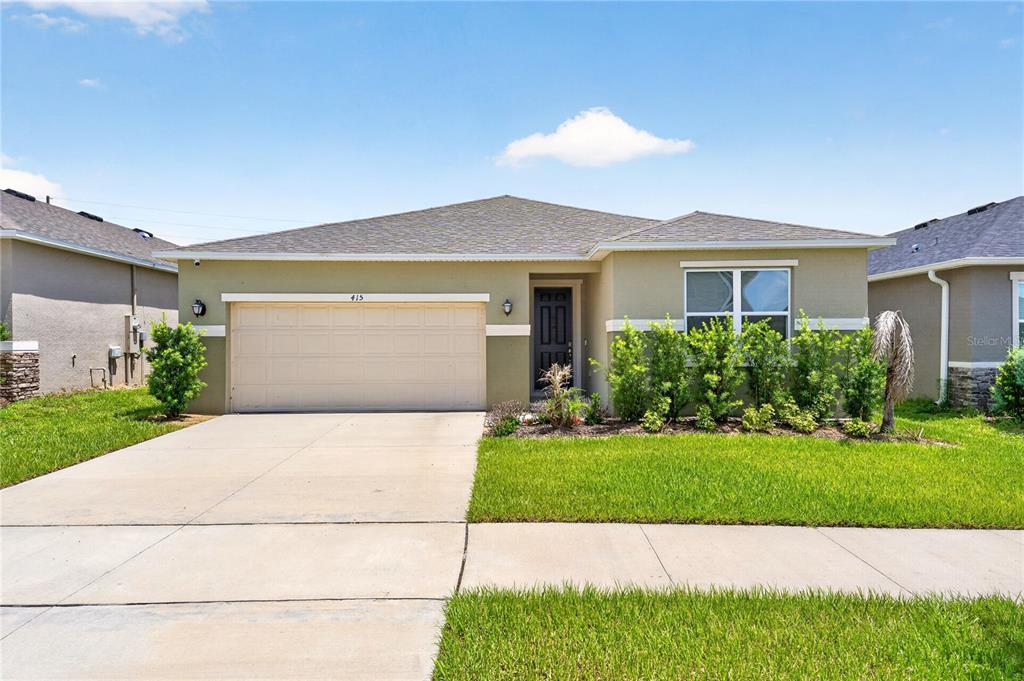 A single-story suburban house with a beige stucco exterior, a two-car garage, and green lawn — 415 OVERPOOL AVENUE, DAVENPORT, FL