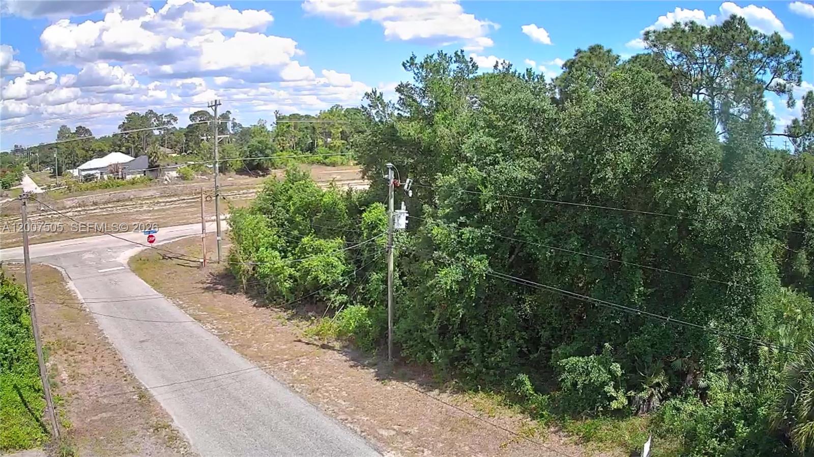 An aerial view shows a paved road, a utility pole, and dense trees on a lot — 3103 45th St SW, Lehigh Acres FL 33976, LEHIGH ACRES, FL