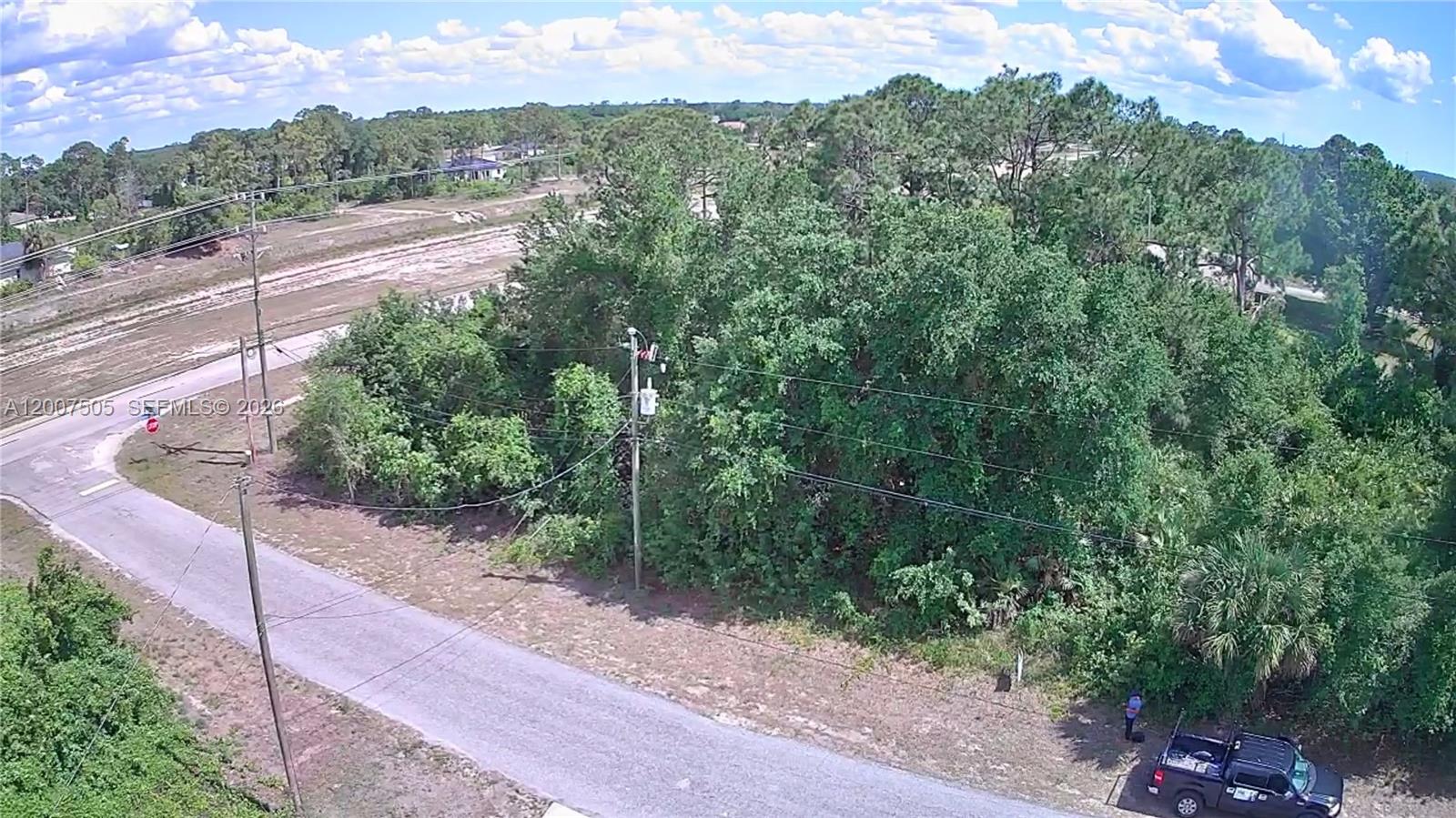 An aerial view shows a wooded lot bordered by a paved road and utility poles — 3103 45th St SW, Lehigh Acres FL 33976, LEHIGH ACRES, FL