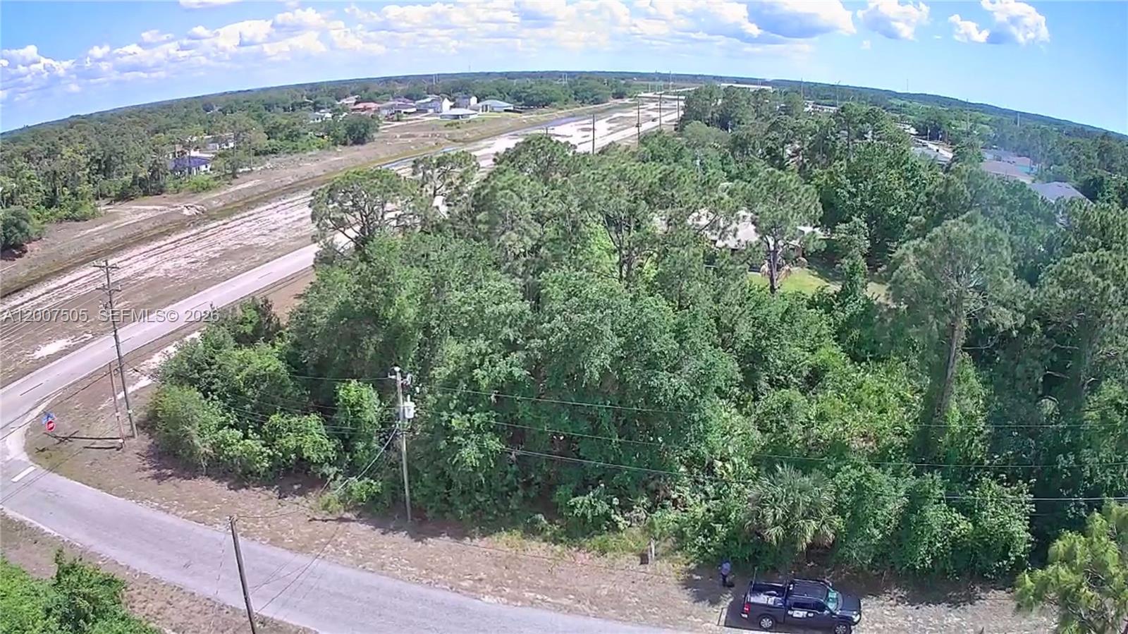 An aerial view shows a wooded lot next to a paved road and a canal — 3103 45th St SW, Lehigh Acres FL 33976, LEHIGH ACRES, FL