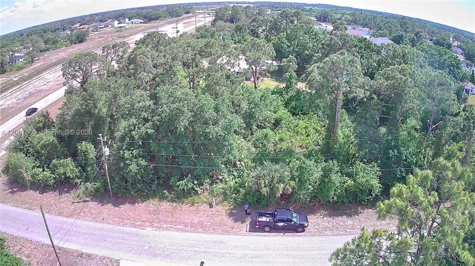 An aerial view shows a wooded lot with a parked truck along a paved road — 3103 45th St SW, Lehigh Acres FL 33976, LEHIGH ACRES, FL