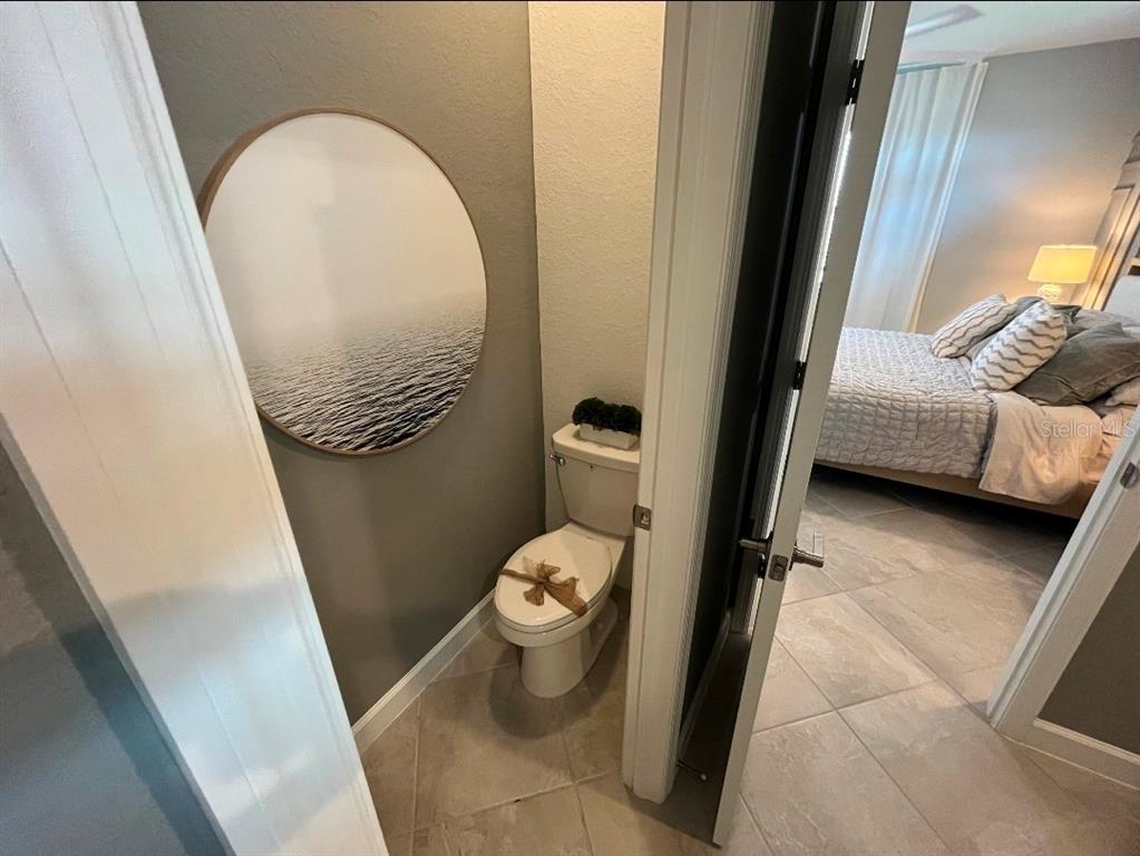 A small bathroom with a round wall art piece sits adjacent to a bedroom — 8141 SHORE LAKE DRIVE, ENGLEWOOD, FL