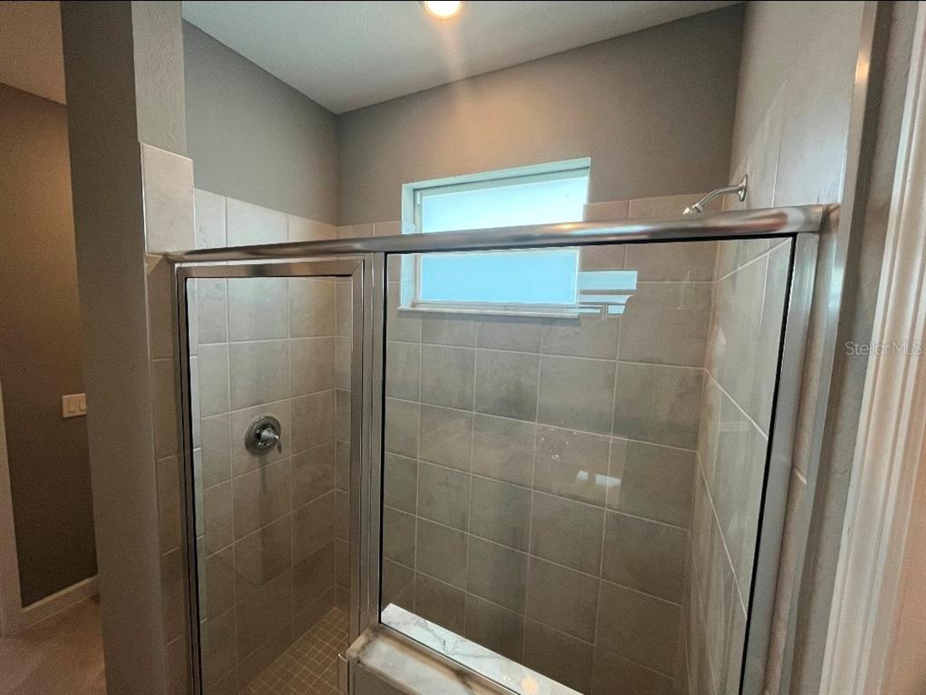 A tiled walk-in shower features a glass door, a window, and a chrome shower head — 8141 SHORE LAKE DRIVE, ENGLEWOOD, FL