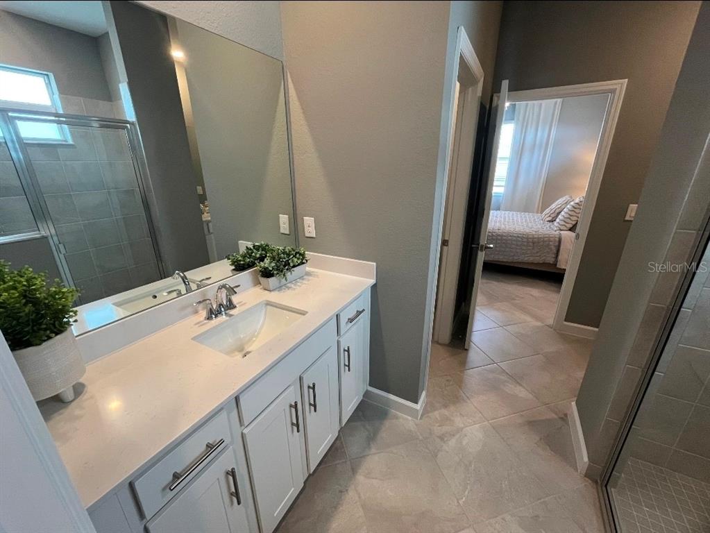 A bathroom with a white vanity, quartz countertop, and tile flooring, looking into a bedroom — 8141 SHORE LAKE DRIVE, ENGLEWOOD, FL