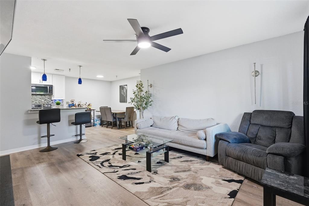 A living room with a grey sofa and recliner, glass coffee table, and open kitchen — 10265 GANDY BOULEVARD N UNIT 1415, ST PETERSBURG, FL
