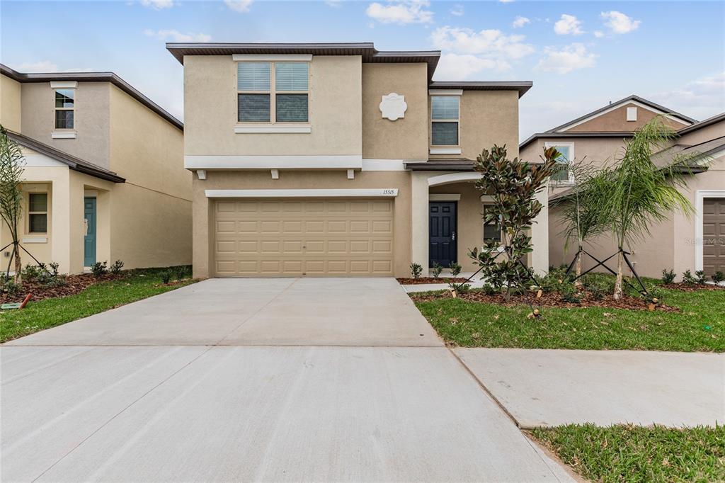 A two-story suburban house features a tan stucco exterior, a two-car garage, and a driveway — 15515 PEACE RIVER PLACE, SUN CITY CENTER, FL