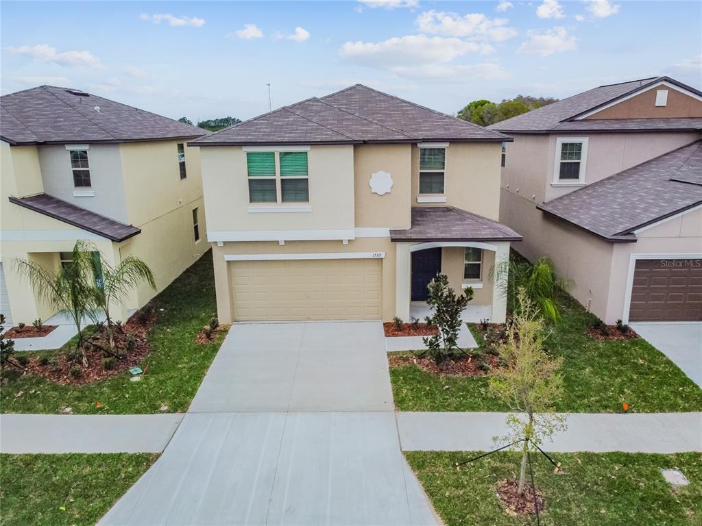 A two-story suburban house with a tan stucco exterior, a two-car garage, and a shingled roof — 15515 PEACE RIVER PLACE, SUN CITY CENTER, FL