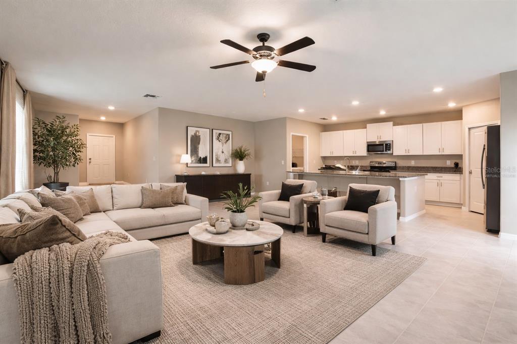 A living room with a sectional sofa and two armchairs opens to a white kitchen — 15515 PEACE RIVER PLACE, SUN CITY CENTER, FL