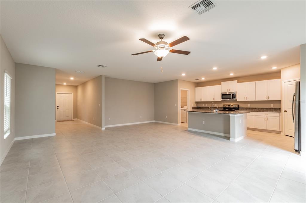 An open-concept living area features light tile flooring, a kitchen island, and white cabinetry — 15515 PEACE RIVER PLACE, SUN CITY CENTER, FL