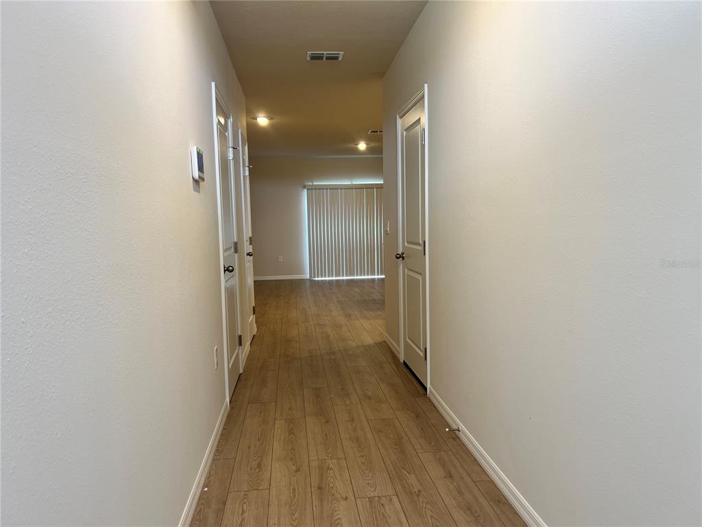 A hallway with wood-look flooring leads to a living area with vertical blinds — 2613 FETLOCK RUN, LAKEWOOD RANCH, FL