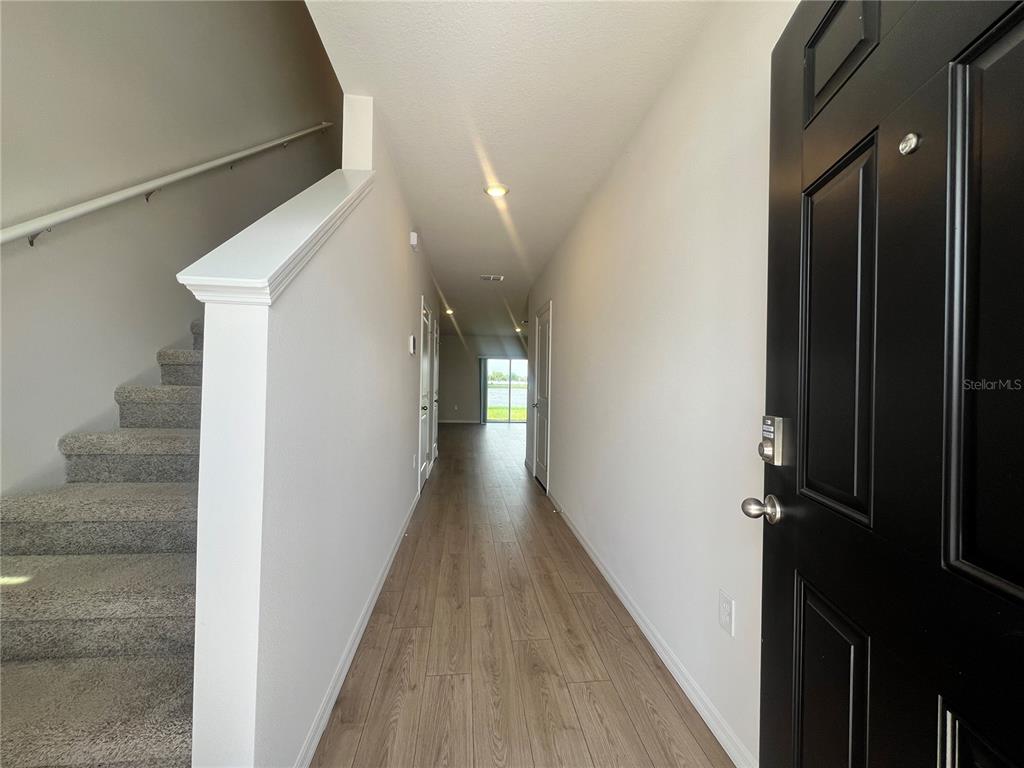 An entryway features wood-look flooring, a carpeted staircase with a handrail, and a black door — 2613 FETLOCK RUN, LAKEWOOD RANCH, FL