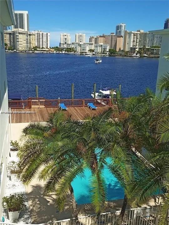 A swimming pool and wooden deck overlook a waterway with boats and city buildings — 462 Golden Isles Dr # 202, Hallandale Beach FL 33009, HALLANDALE BEACH, FL