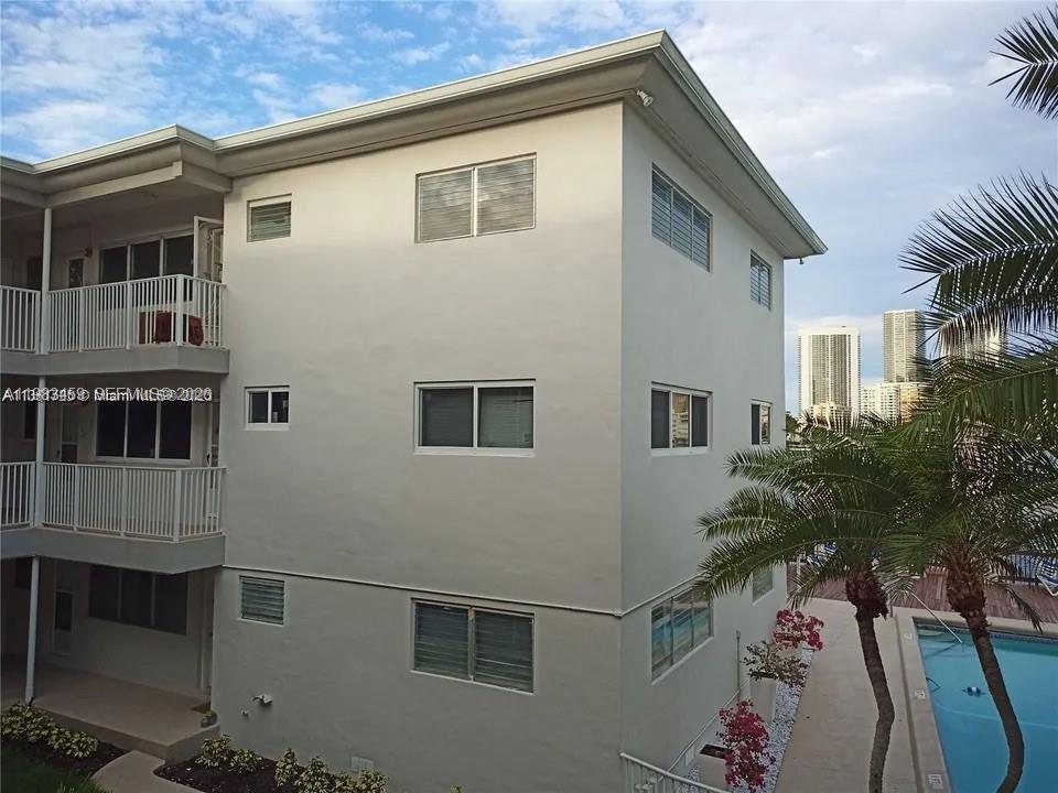 A three-story apartment building exterior features white walls, multiple windows, and an adjacent swimming pool — 462 Golden Isles Dr # 202, Hallandale Beach FL 33009, HALLANDALE BEACH, FL