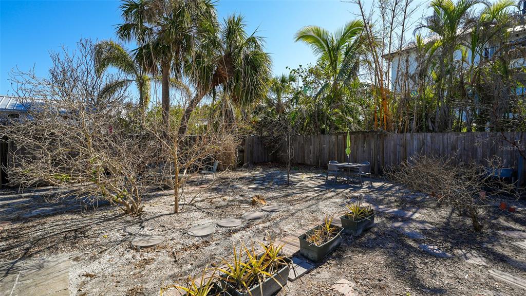 A backyard area features a wooden fence, sparse landscaping, potted plants, and a small patio table — 132 HARRISON DRIVE, SARASOTA, FL