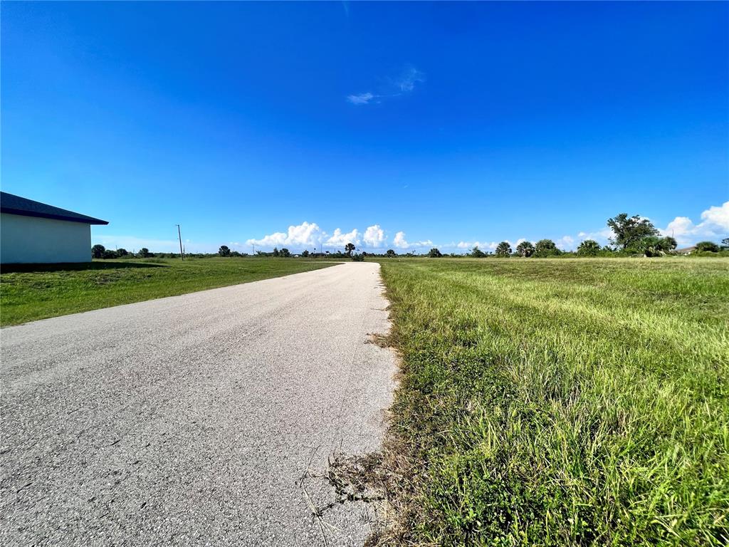 A paved road stretches through an open, grassy field under a clear blue sky — 3833 NW 38TH AVENUE, CAPE CORAL, FL
