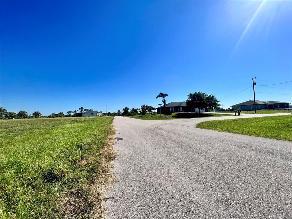 A paved road forks through a grassy, open lot under a clear blue sky — 3833 NW 38TH AVENUE, CAPE CORAL, FL