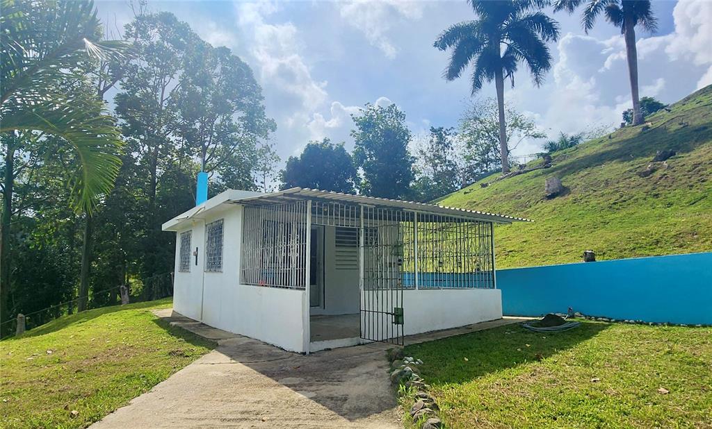 A small white house with a metal-caged porch sits on a grassy hillside — KM 12.2 INT LAS PAPAYAS RD (SR-185) Lots A and B, CAROLINA, PR