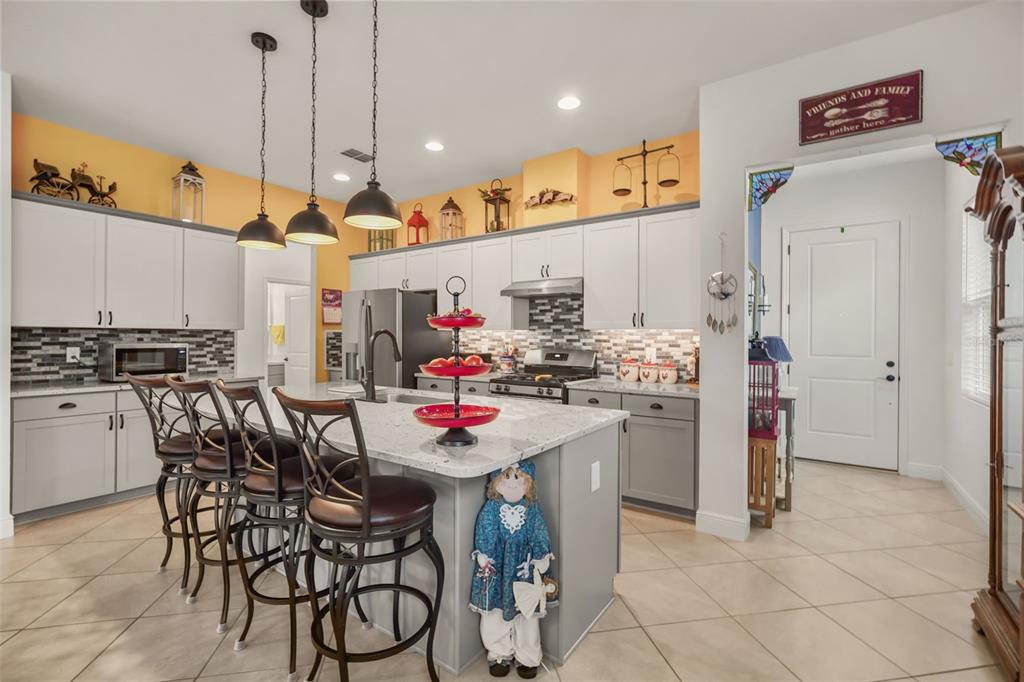 A kitchen features gray cabinetry, a granite-topped island with bar stools, and yellow upper walls — 1667 KEY BAY TRAIL, KISSIMMEE, FL
