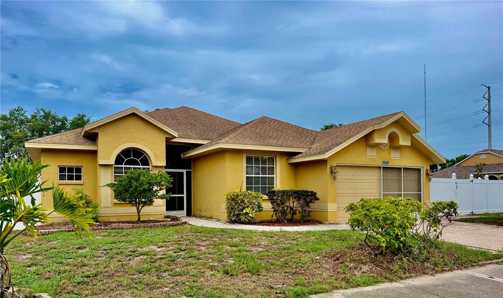 A yellow, single-story suburban house with a brown shingled roof and a two-car garage — 1959 WOOD TRAIL STREET, TARPON SPRINGS, FL