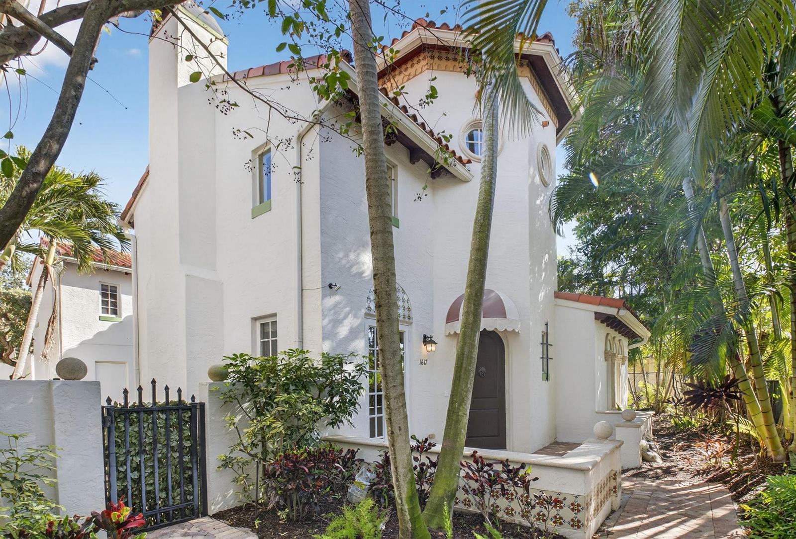 A two-story white Mediterranean-style house features a tiled roof, arched doorway, and lush landscaping — 1617 Estuary Way, Delray Beach FL 33483, DELRAY BEACH, FL