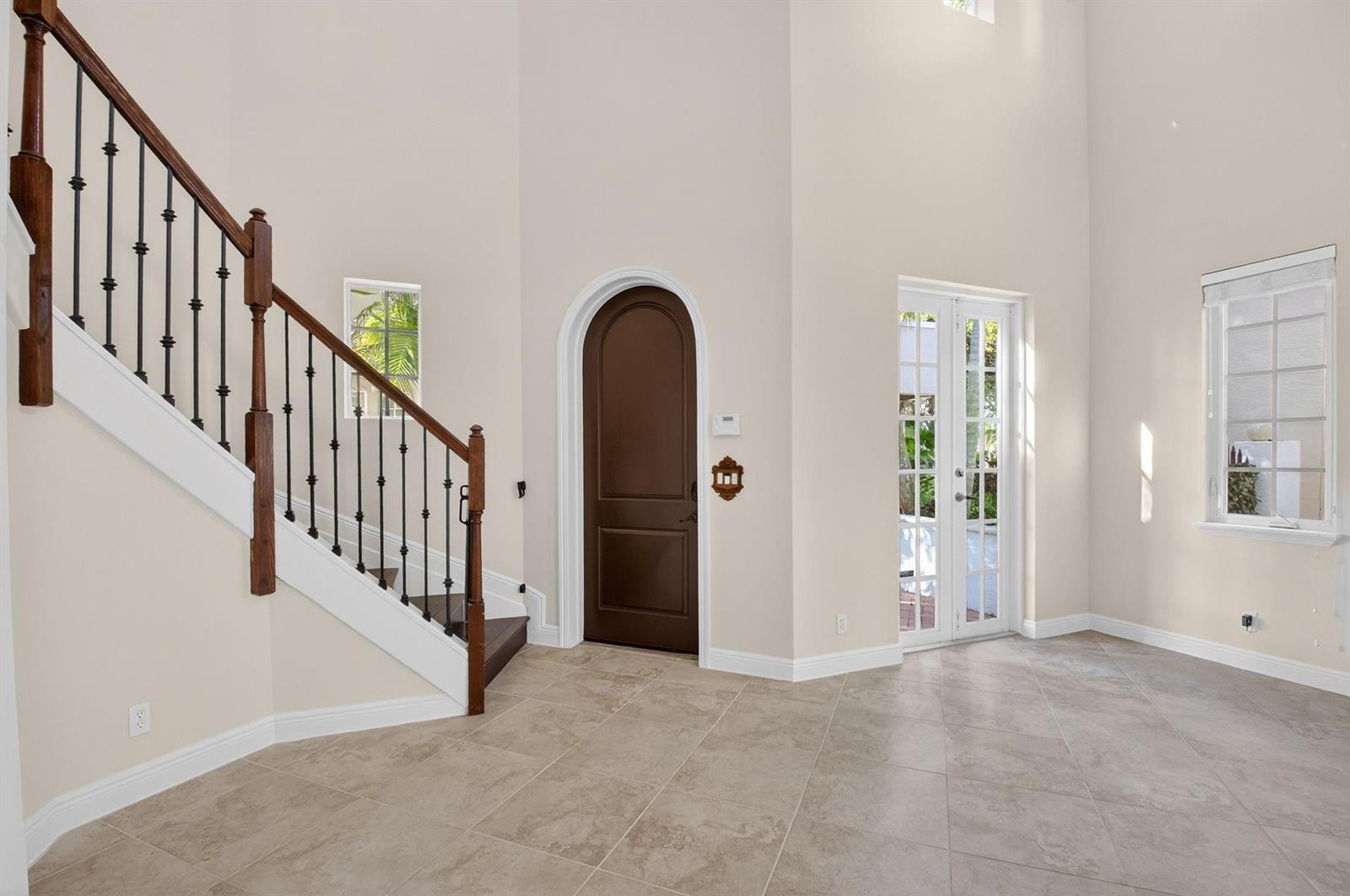An entryway features a staircase with iron railings, a dark arched door, and tiled floors — 1617 Estuary Way, Delray Beach FL 33483, DELRAY BEACH, FL