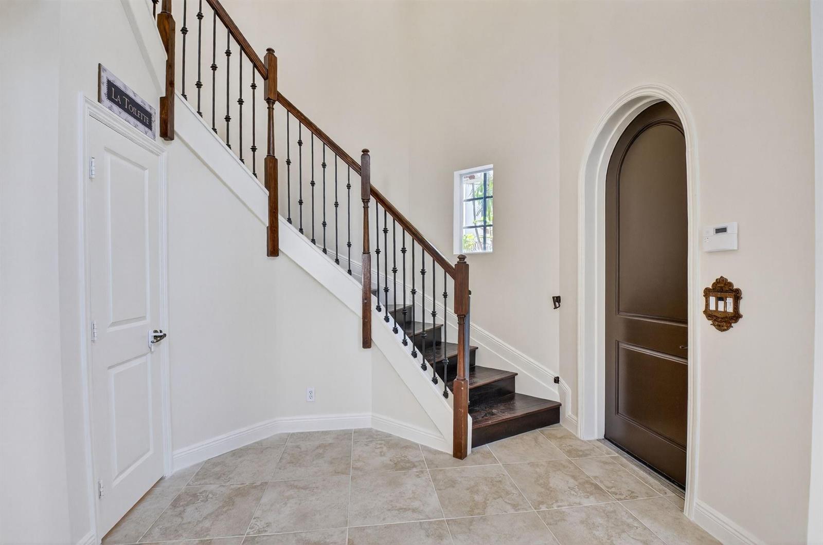 A foyer features a tiled floor, a staircase with dark wood treads, and an arched doorway — 1617 Estuary Way, Delray Beach FL 33483, DELRAY BEACH, FL