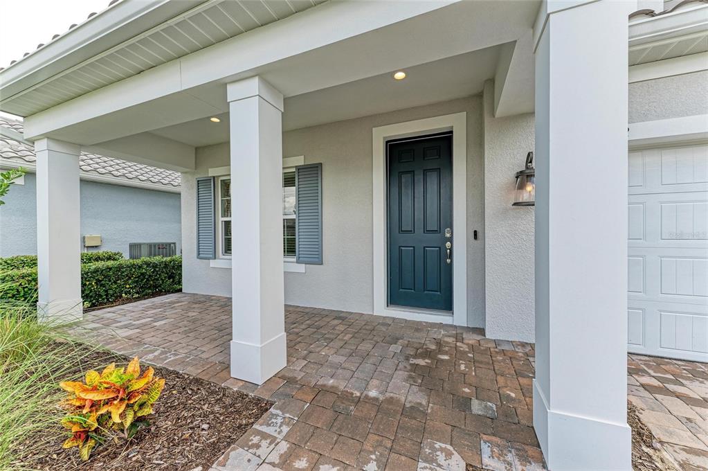 A covered front porch with brick pavers leads to a dark blue front door — 2802 BUTTERFLY JASMINE TRAIL, SARASOTA, FL