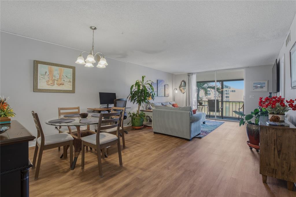 An open-concept living and dining area features wood-look flooring, a glass table, and balcony access — 7540 BAY ISLAND DRIVE S UNIT 251, SOUTH PASADENA, FL