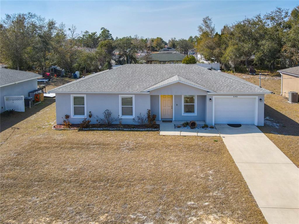 A single-story house with a gray exterior, a yellow front door, and a concrete driveway — 640 CHESTNUT AVENUE, ORANGE CITY, FL