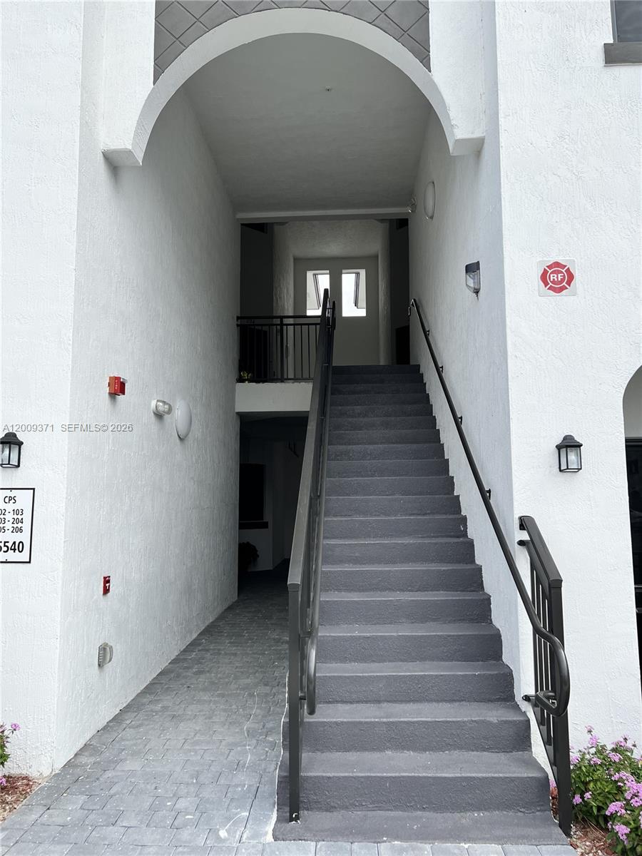 An exterior staircase with dark railings leads to an upper-level landing under an arched entryway — 15540 SW 136th St # 206, Miami FL 33196, MIAMI, FL