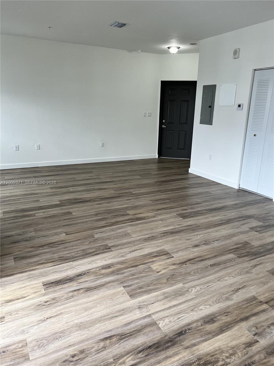 An empty room features wood-look flooring, white walls, a black door, and a closet — 15540 SW 136th St # 206, Miami FL 33196, MIAMI, FL